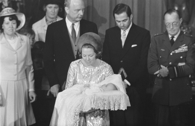 Königin Elizabeth II wiegt ihren neugeborenen Sohn Prinz Philip, während Prinz Philip, Herzog von Edinburgh, neben ihr in einem Anzug und Krawatte steht, mit Vorhängen im Hintergrund.