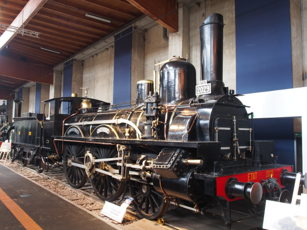Alte Dampflokomotive in einem Museum ausgestellt, umgeben von Eisenbahnschienen, Informationsschildern, St├Ąnden und anderen Ausstellungsstücken.