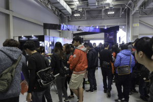 Menschen vor einer Menschenmenge auf einer Gaming-Messe mit Texttafeln, Lichtern und Deckenrohren.