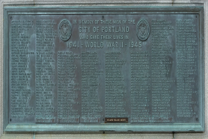 Bronzeplatte an einer Gebäudewand mit der Inschrift "Denkmal für die Stadt Portland" in fetter schwarzer Schrift, eingerahmt von einem dekorativen Rand.