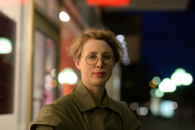 Eine Frau mit Brille steht vor einem Geschäft mit Lichtern und anderen Gegenständen im Hintergrund.