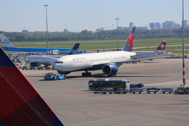 Ein Boeing 777-300ER der Delta Air Lines am Frankfurter Flughafen geparkt, umgeben von Fahrzeugen und Straßenlaternen, mit Gebäuden, Bäumen und einem klaren blauen Himmel im Hintergrund.