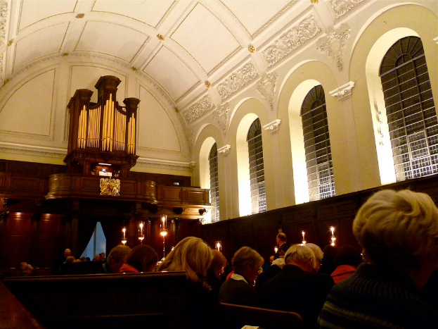 Das Innere einer Kirche mit sitzenden Menschen und Kerzen davor, mit weißen Wänden und Dach.