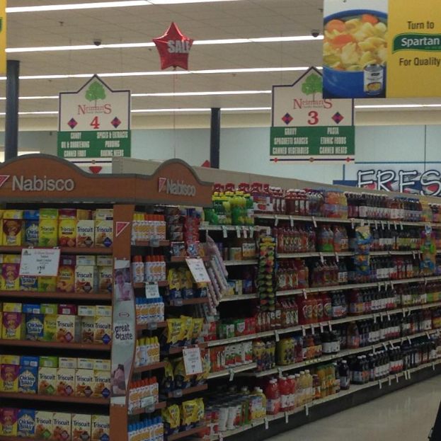 Ein Supermarkt-Innere mit Regalen voller Lebensmittel, Deckenlampen und Schildern.