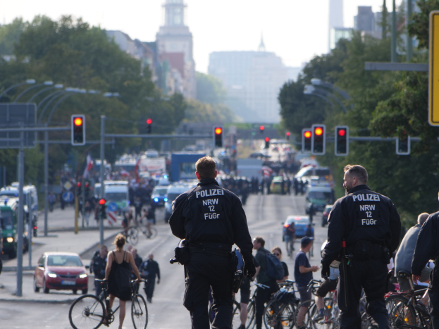 Polizeibeamte auf Fahrrädern eine Straße mit Bäumen, Gebäuden und einem klaren blauen Himmel im Hintergrund entlangfahren.