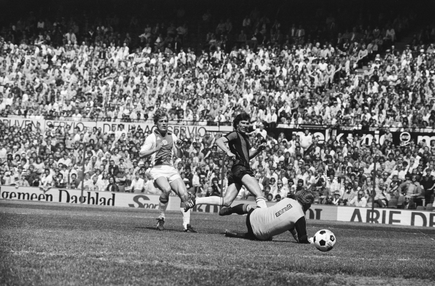 Ein Schwarz-Weiß- Bild von einer Gruppe von Männern, die auf einem Feld Fussball spielen, mit Zuschauern im Hintergrund und einem Banner mit der Aufschrift "Bundesliga 1978-79 Ajax 1-1 Hannover 96."