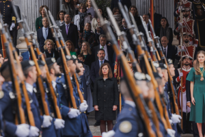 Eine Gruppe von Menschen in militärischer Kleidung steht vor einem Publikum, einige Zuschauer halten Gewehre in der Hand.
