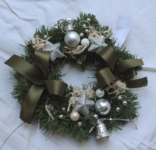 Ein festliches Weihnachtsgesteck mit Silberornamenten und Bändern auf einem weißen Tuch, mit bunten Kugeln, Sternen und anderen Dekorationen.