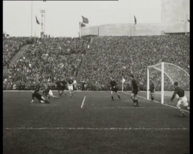 Ein Schwarz-Weiß-Foto eines Fußballspiels im Stadion, mit Spielern auf dem Feld und einem Torpfosten auf der rechten Seite, Zuschauern auf den Tribünen und Fahnen mit Stangen im Hintergrund, mit Text oben und unten: "1958-1958 WM-Finale - Manchester United vs. Liverpool."