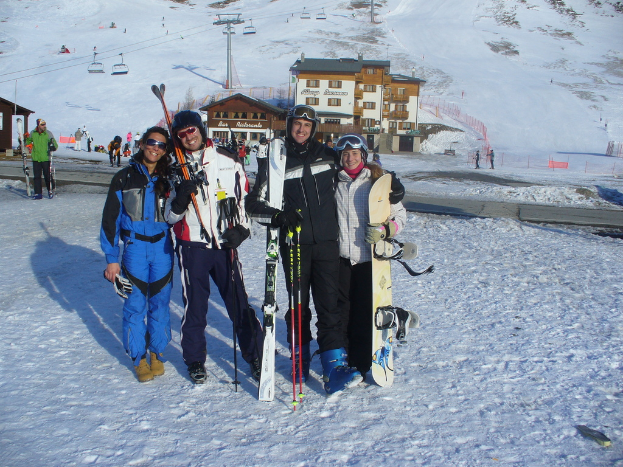 Vier Personen posieren für ein Foto mit Skate-Pads und Werkzeugen im Hintergrund vor einer schneebedeckten Berglandschaft.