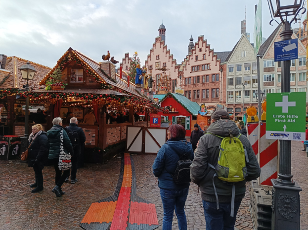 Menschen auf einem Kopfsteinpflasterweg neben einem Weihnachtsmarkt in Nürnberg, Deutschland, mit Laternen und Infotafeln im Blick.