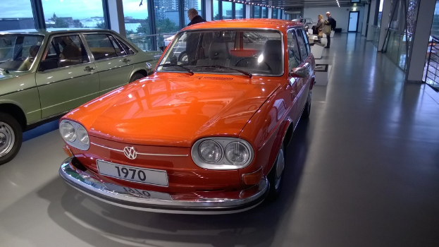 Zwei orange und grüne Autos stehen mit Menschen und Bäumen im Hintergrund durch ein Fenster sichtbar.