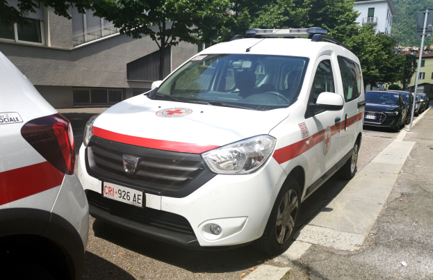 Zwei Ambulanzen nebeneinander auf einer Straße geparkt, mit Gebäuden, Bäumen und Polen im Hintergrund unter einem klaren blauen Himmel.