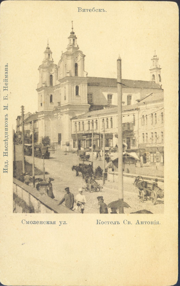 Ein altes Foto einer belebten Stadtstraße mit einer Kirche im Hintergrund, das Gebäude, Pfähle, Menschen, Karren, Pferdefuhrwerke und Bäume an der Straße zeigt, mit Text am unteren Rand des Bildes.
