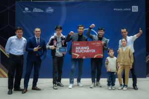 Gruppe von Menschen auf einer Bühne mit einer Tafel, auf der 'Akang Kuchaydi - Zakovat Quiz' steht, im Hintergrund ein Banner und Lichter.