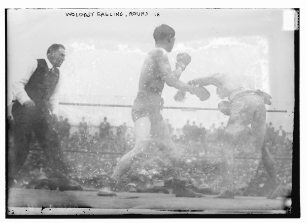Ein Schwarz-Weiß-Foto von zwei Boxern in einem Ring, mit einem Mann links und Zuschauern im Hintergrund und Text oben.