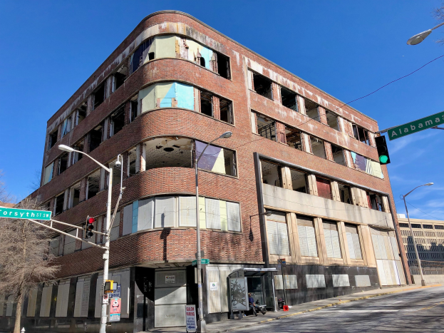 Altes Backsteingebäude an einer Straßenkreuzung, als ehemaliger Hauptsitz der University of Illinois at Chicago markiert, mit Straßeninfrastruktur, Fahrzeugen, Bäumen und einem bewölkten Himmel.
