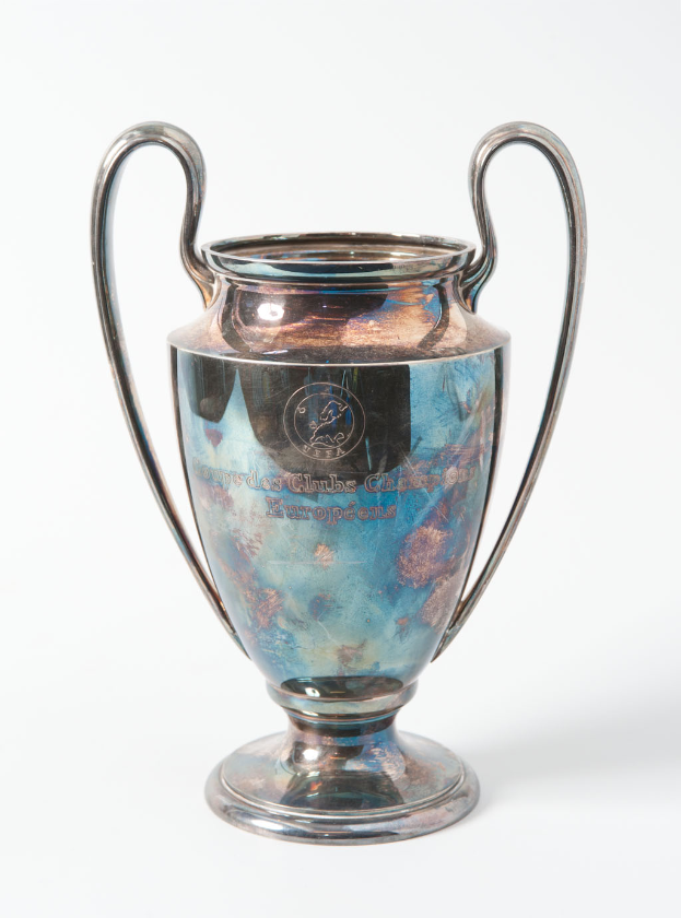 Der UEFA-Champions-League-Pokal, ein stählerner Becher mit zwei Griffen und einem blauen und silbernen Farbschema, mit der Inschrift "UEFA Champions League", vor einem weißen Hintergrund.