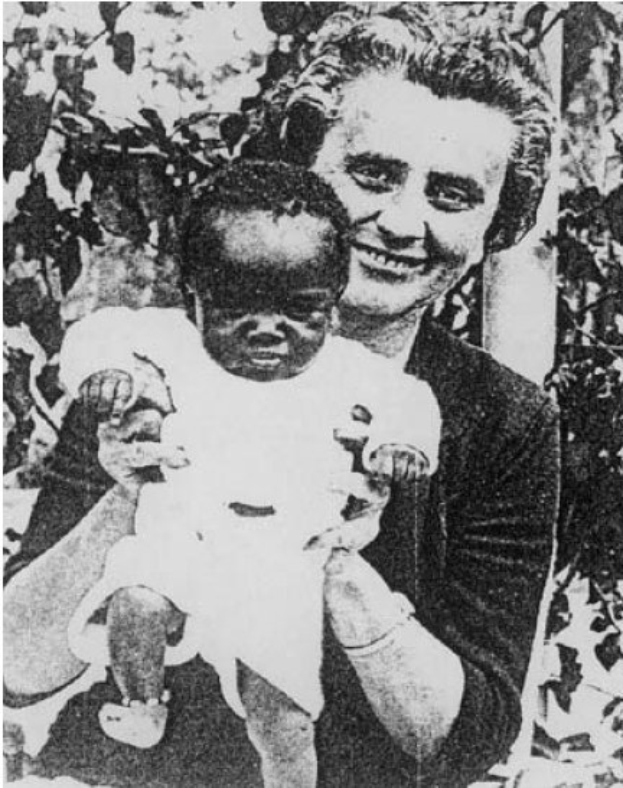 Ein Schwarz-Weiß-Foto einer Frau, die lächelt, während sie ein Baby hält, mit Blättern im Hintergrund