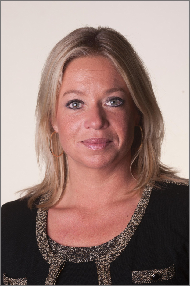 Eine Frau mit blonden Haaren in einem ordentlichen Dutt, die ein schwarzes Kleid und goldene Kreolen trägt und warm und lebhaft lächelt.
