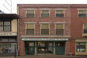 Ladenfront von "Residences at Market at Fifth" mit Glasfenstern und -türen, die Schaufensterpuppen in Kleidern zeigen, vor einem Straßen- und Himmel-Hintergrund.