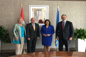 Eine Gruppe strahlender Menschen, die um einen Tisch mit Papieren stehen, umgeben von Fahnen, Topfpflanzen und einem Fotorahmen an der Wand, feiern die Unterzeichnung eines Memorandums von Verständnis zwischen den Vereinigten Staaten und Kanada.