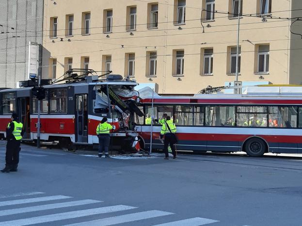 Rote und weiße Tram war in einen Unfall auf der Straße verwickelt, mit Menschen in der Nähe und einem Gebäude im Hintergrund.