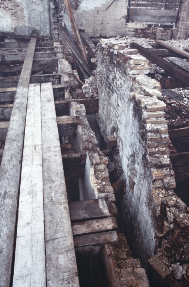 Ein altes Gebäude mit Schutt aus Holzplanken und Steinen auf dem Boden, mit einer Wand im Hintergrund, die den Abriss anzeigt.
