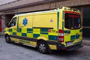 Ambulanz auf der Straße vor einem Backsteingebäude mit Text geparkt, mit einem Feuerlöscher auf seiner linken Seite.