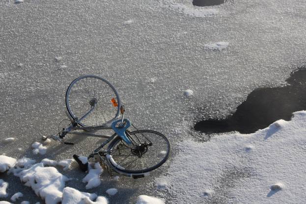 Ein Fahrrad liegt im Schnee neben einer Pfütze Wasser, mit einer Schneedecke drum herum.