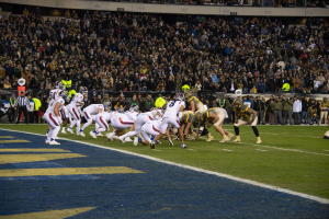 Fußballspieler mit Helmen und Uniformen auf dem Boden während eines Spiels in einem Stadion mit Zuschauern und Tafeln im Hintergrund.