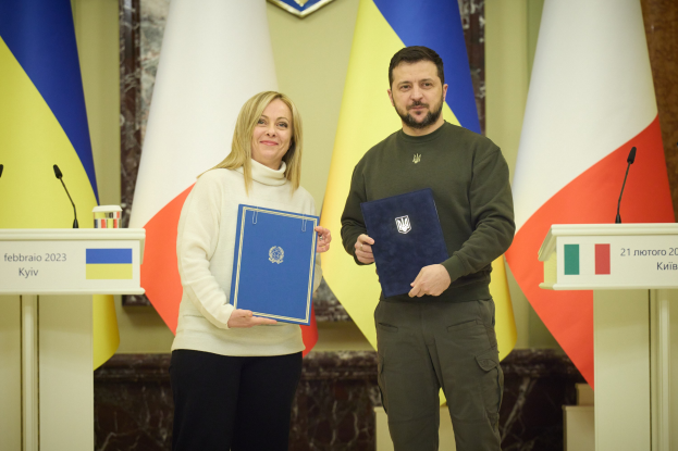 Zwei Personen lächeln neben Rednerpulten mit Mikrofonen, halten Bücher in der Hand, vor Flaggen und einer mit Logo verzierten Wand - Symbol für eine Vereinbarung zwischen Ukraine und Polen.
