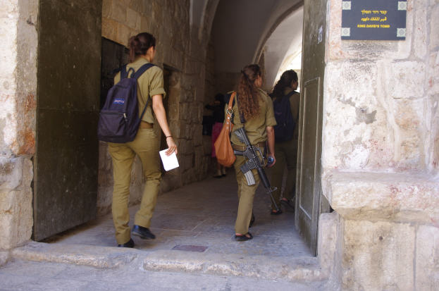 Israeli Soldaten in Uniform durchschreiten einen Torbogen in Jerusalems alter Stadt, einer hält eine Waffe und ein Blatt Papier, mit einer Tafel an der Wand rechts.