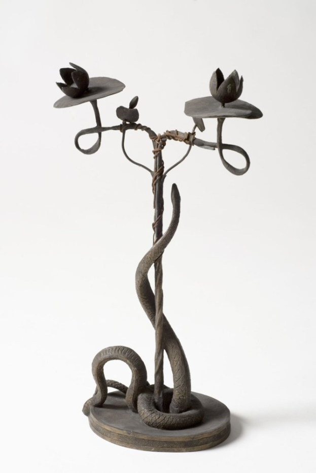 Eine Metallskulptur einer Schlange, die sich um einen Kerzenhalter mit drei Blumen windet, vor einem weißen Hintergrund.