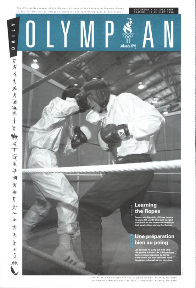 Zwei Boxer im Ring, mit Helmen und Handschuhen, Seilen und Lichtern und dem Text "Olympian Magazine" oben und unten.