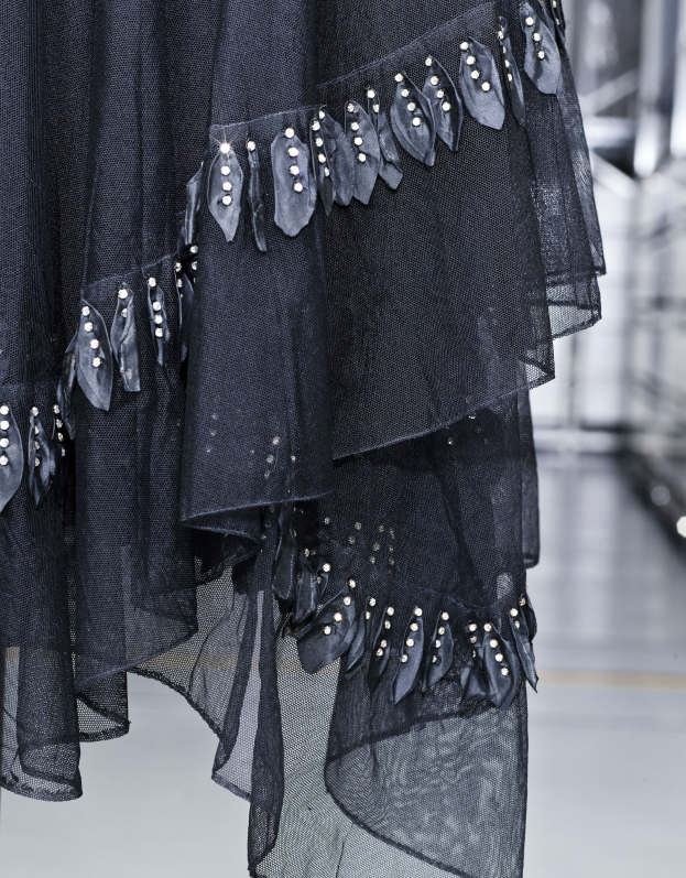 Schwarzes bodenlanges Kleid mit hohem Ausschnitt, langen Ärmeln und vollem Rock, mit aufwendiger Perlen- und Paillettenverzierung auf leichtem Stoff mit feiner Schimmer, präsentiert auf dem Laufsteg.