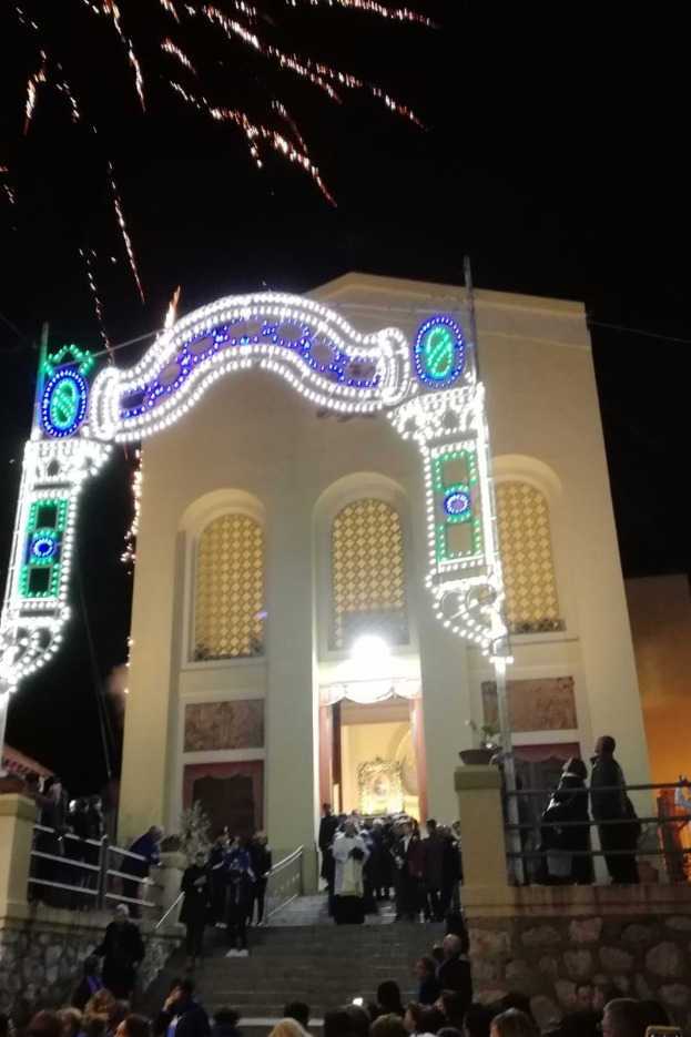 Menschen vor einem Gebäude mit einem beleuchteten Bogen, Treppe und Topfpflanzen während einer Silvesterfeier mit Feuerwerk am Himmel.