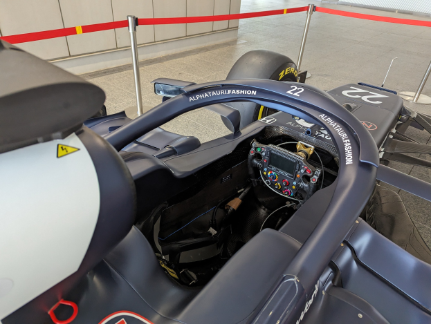 Cockpit eines Formel-E-Autos in einer Ausstellung, Lenkrad im Vordergrund, Wand und gesäumte Stangen im Hintergrund.