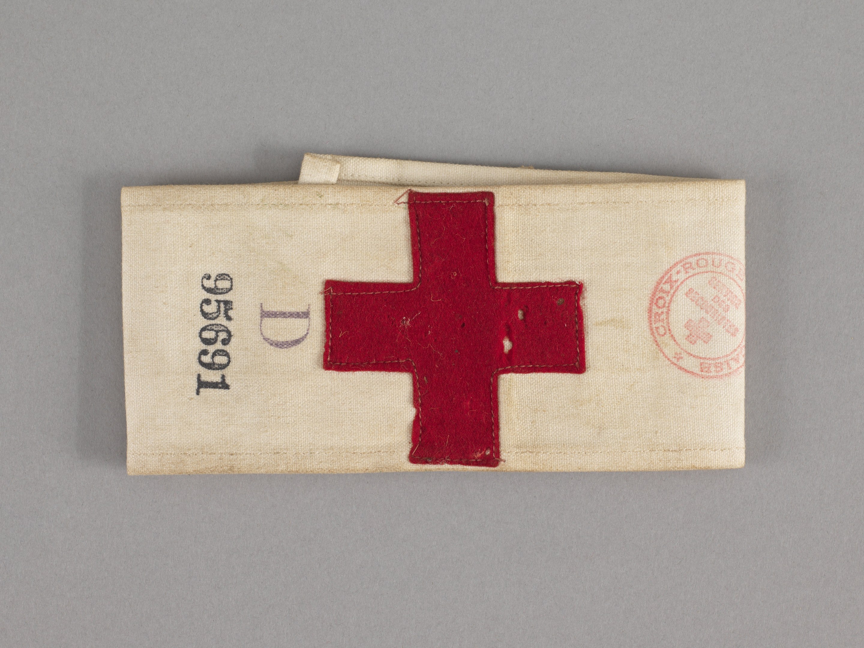 Ein rotes Kreuz-Ersthelfer-Set in einer Stofftasche mit Text und einem Stempel, das auf einer Oberfläche liegt.