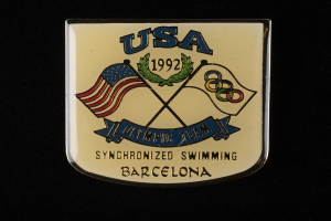 Abzeichen mit 'USA Olympische Mannschaft Synchronschwimmen Barcelona' Text und zwei Flaggen (rot und blau) auf schwarzem Hintergrund.