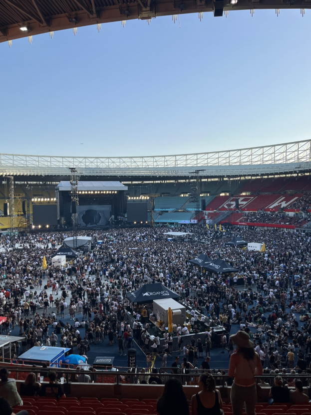 Große Menschenmenge auf Sitzplätzen und Stehplätzen in einer Halle mit Geländern, Zelten und Deckenbeleuchtung, was auf ein Konzert in der O2 Arena in London hindeutet.