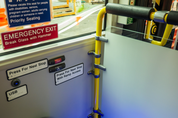 Notausgangsschild an der Seite eines Zuges mit einer Tür, Griff und Glasfenster, das die Straße und Pfosten zeigt.