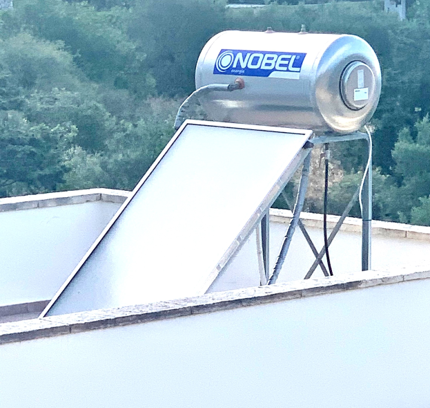 Solarwassererhitzer mit Speicher auf einem Gebäude Dach montiert, Bäume im Hintergrund sichtbar.