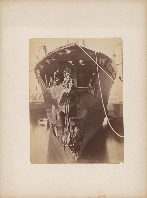 Ein altes Schwarz-Weiß-Foto eines Bootes im Wasser mit ein paar Menschen darauf, umgeben von verstreuten Werkzeugen und Materialien, das eine Reparatur des Bootes vermuten lässt.