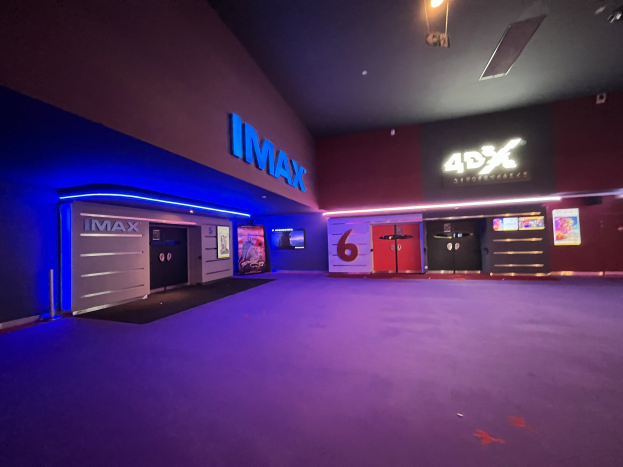 Innenansicht eines Kinos mit lila Teppichboden, Wänden mit Text und Bildschirmen sowie Deckenbeleuchtung.