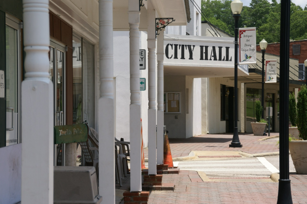 Rathaus mit umliegenden Gebäuden, Straßeninfrastruktur, Kraftfahrzeugen, Verkehrskegeln, Möbeln, Grünpflanzen und einem bewölkten Himmel.