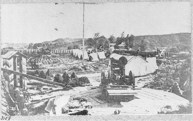 Schwarzes und weißes Foto einer Baustelle mit einer Maschine im Vordergrund, Schuppen, Bäumen, Höhen und Himmel im Hintergrund, mit Text unten, der "Die Konstruktion einer neuen Brücke in der Stadt San Francisco, Kalifornien." lautet.