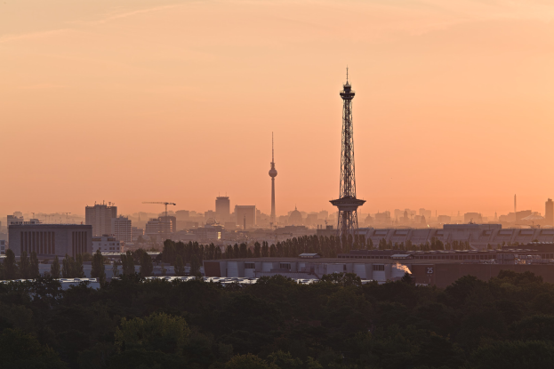 Sunset view of Berlin skyline from a hilltop, featuring buildings, trees, and the TV Tower in the background with a colorful sky.