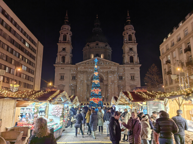 Weihnachtsmarkt mit beleuchteten Buden vor einer Kirche bei Nacht, Menschen schlendern, Gebäude und Bäume im Hintergrund unter einem sternenklaren Himmel.