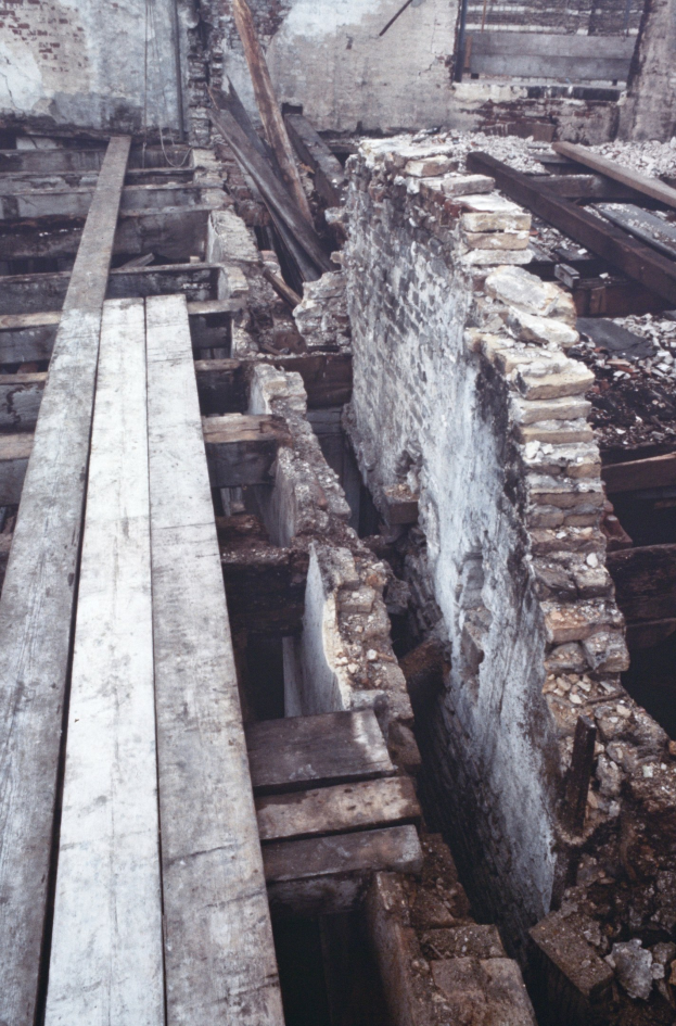 Altes Gebäude im Abriss mit verstreuten Holzplanken und Steinen und einer sichtbaren Wand im Hintergrund.